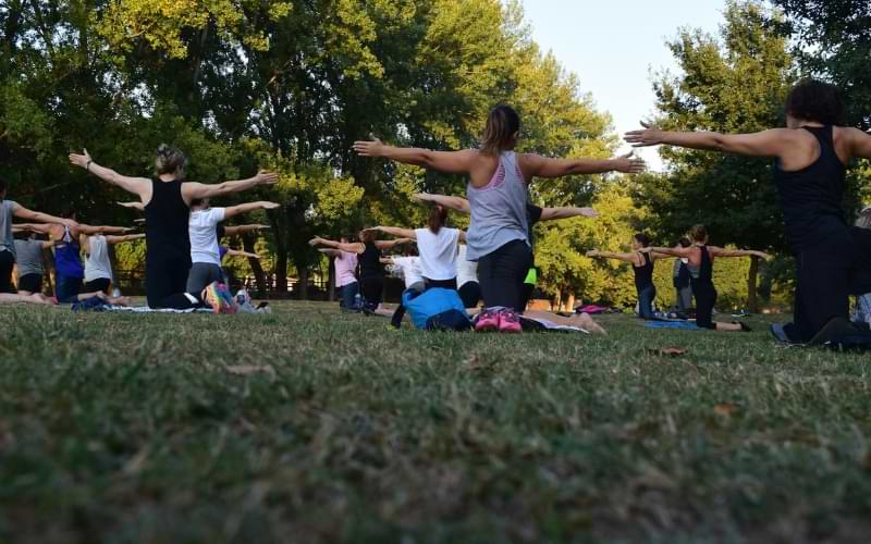 A group of people doing a yoga class outside. There are trees beyond them in the distance.