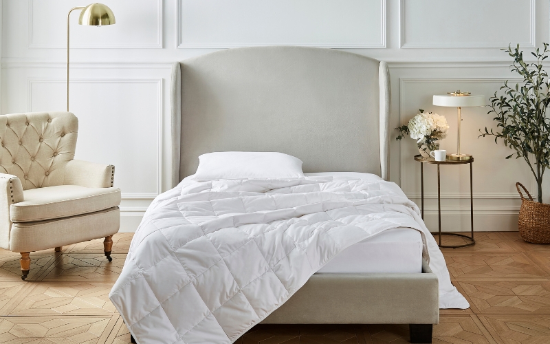 A Liddell cashmere duvet draped across a mattress, half hanging off. It's in a contemporary bedroom with a huge headboard. A lamp and a plant sits to one side. Another lamp and a chair is off to the other side. 